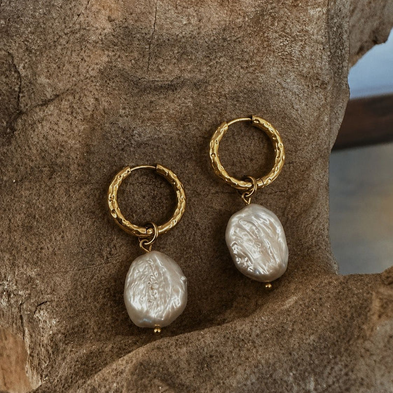 Gold hoop earrings with pearl drops on a stone surface