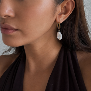 A close-up of a model wearing a gold hoop earring with a dangling fresh water pearl.
